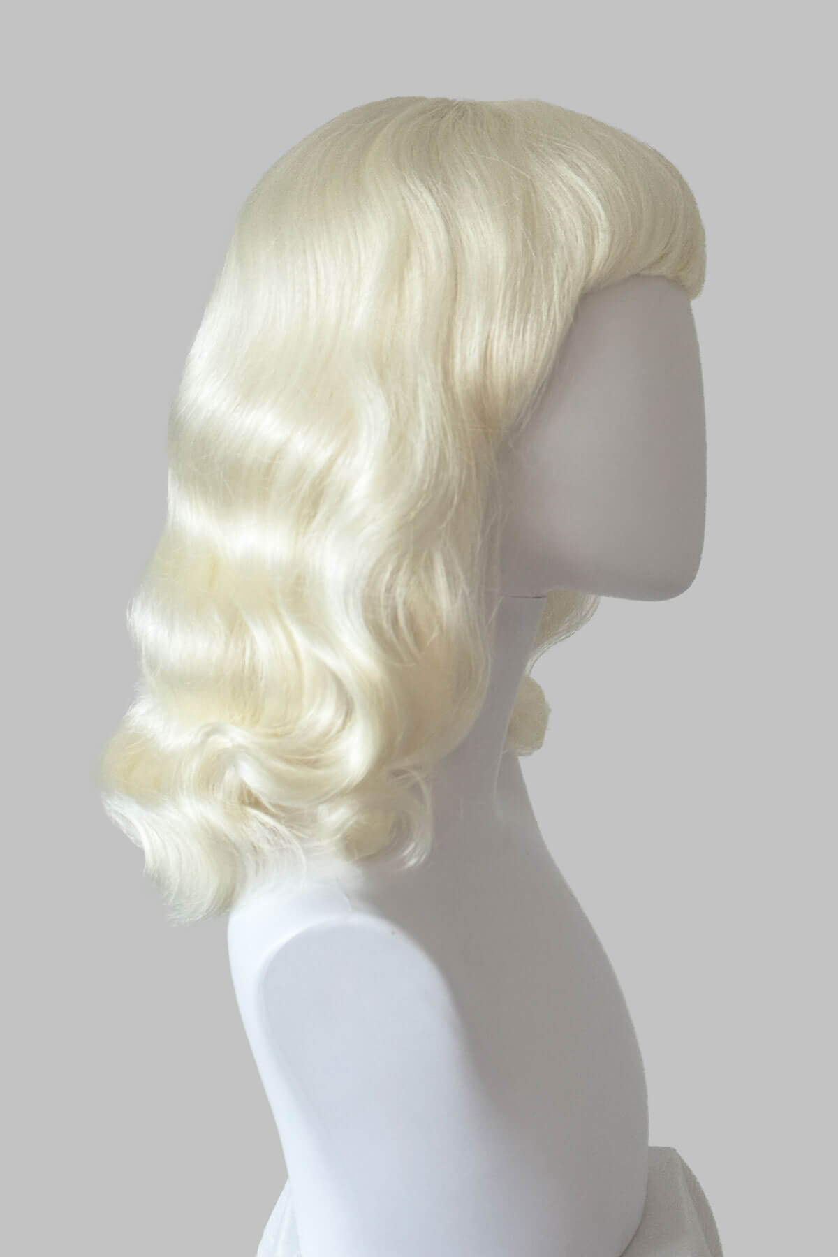 Blonde wig on a mannequin head against a plain background. Platinum blonde pin-up style wig with short fringe and marcel waves: Eira