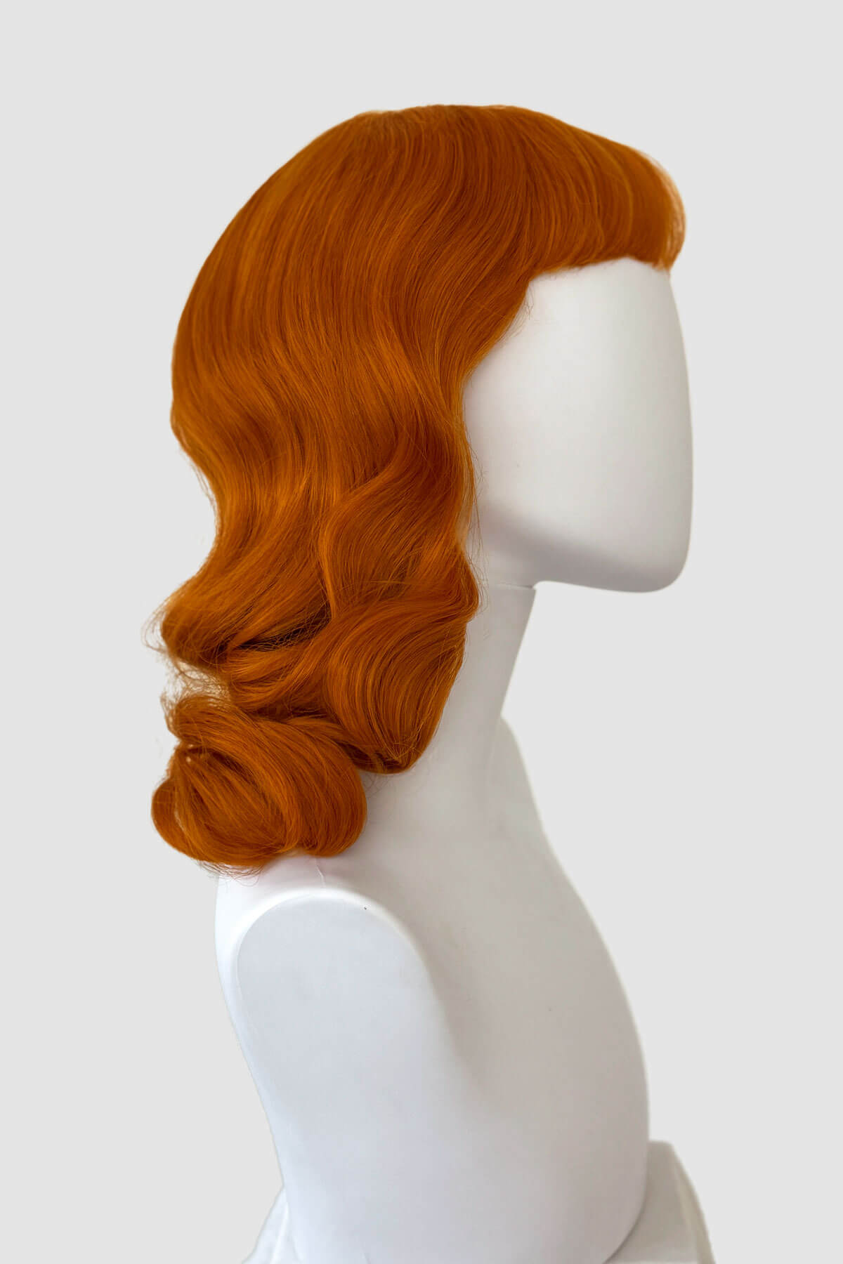 Ginger red wig on a mannequin head against a white background. Ginger pinup style wig, finger waved with short fringe: Sienna