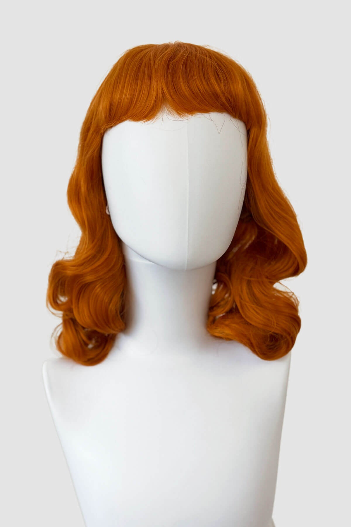 Ginger red wig on a mannequin head against a white background. Ginger pinup style wig, finger waved with short fringe: Sienna