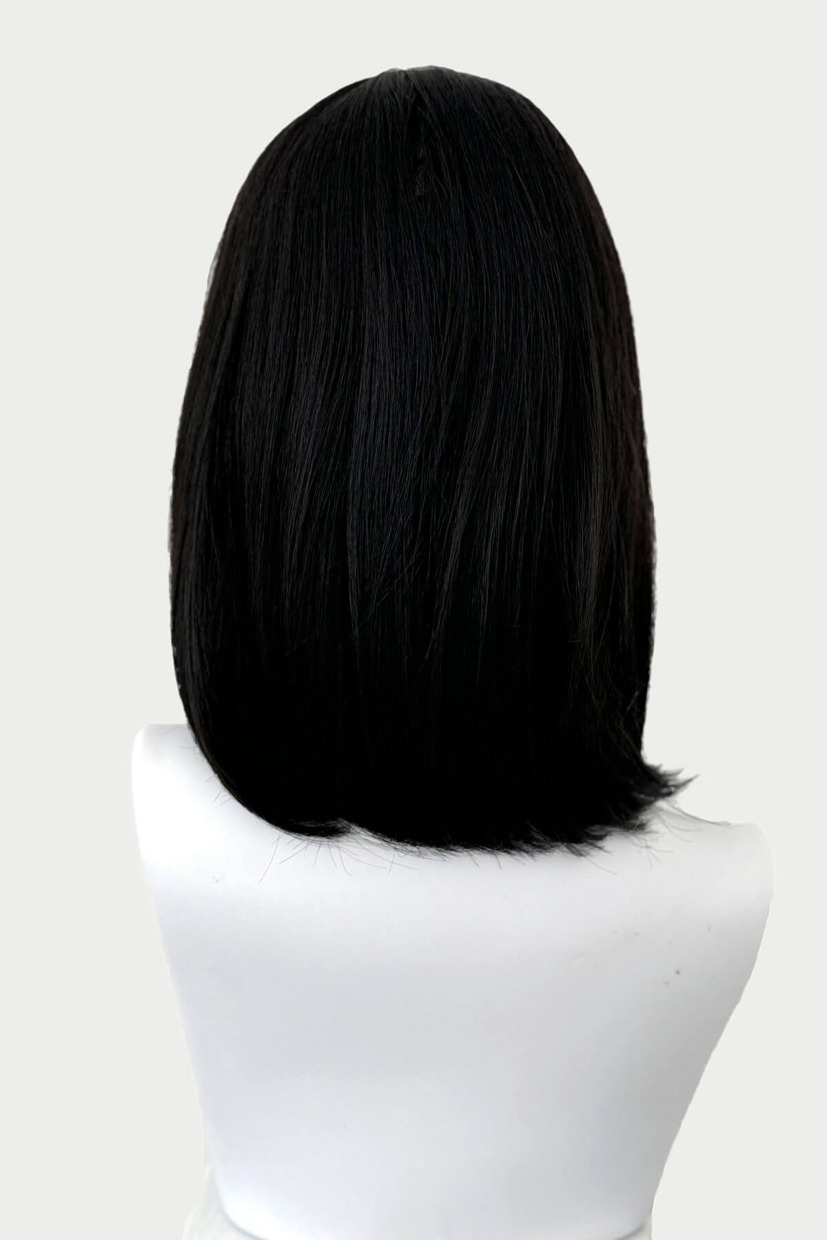 Black wig on a mannequin head against a white background. Black long bob wig with a short retro, rockabilly-style fringe: Beth