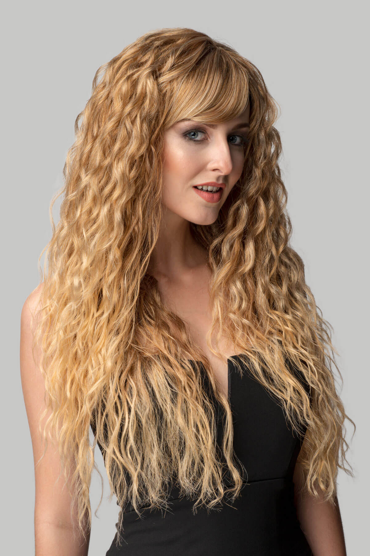 Woman with long, wavy blonde hair against a gray background. Long brown crimped wig, brown and blonde dip dye (ombre): Tiggy