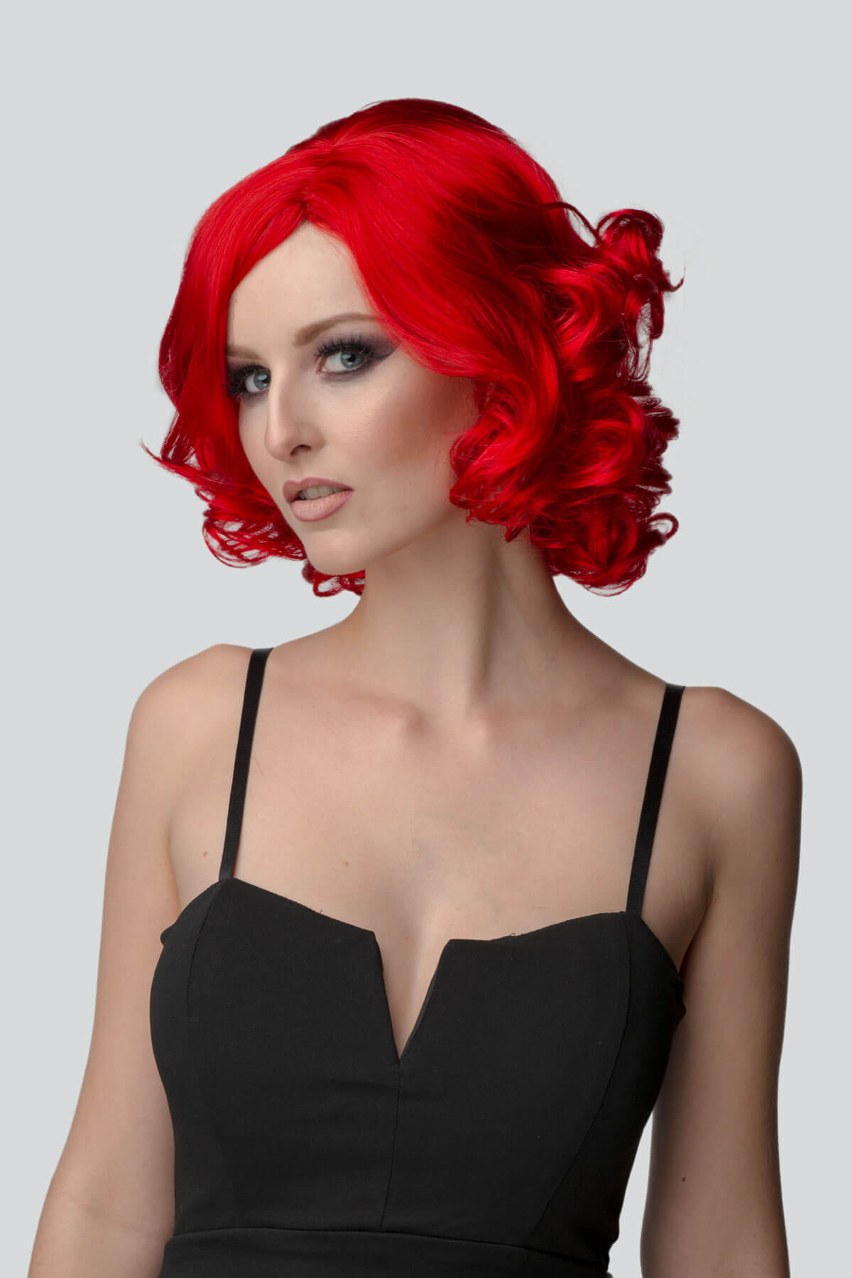 Woman with red wig and black dress on gray background. Rihanna style red wig, short with curls: Rihanna