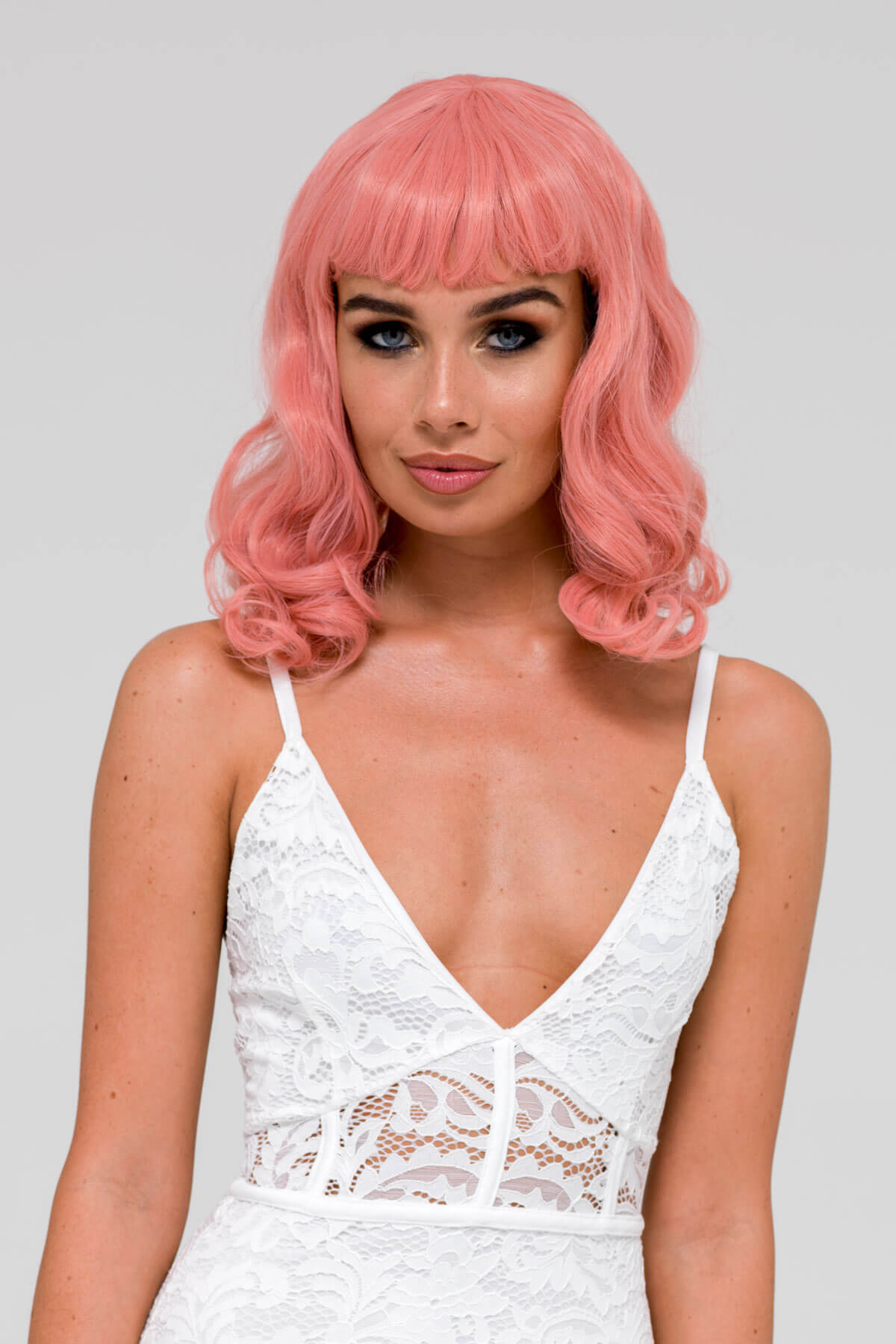 Woman with pink wig and white lace top on a gray background. Pink pinup style wig, with finger waves and a short fringe, 1950s style: Stevie