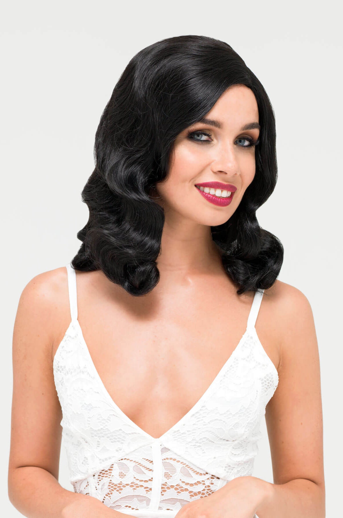Woman with styled black hair wearing a white lace top on a light gray.background. Black 1930s style wig with long marcel waves: Vivienne