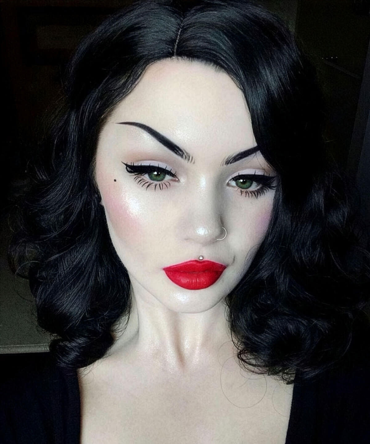 Person with dramatic makeup and black hair against a dark background. Black 40s style wig with beautiful marcel waves: Dita