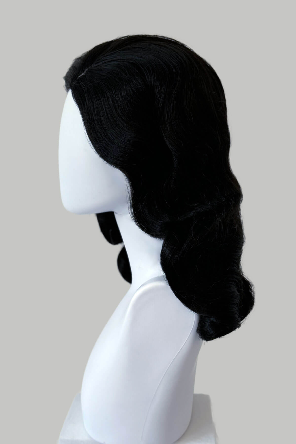 Black wig on a white mannequin head against a plain background. Black 1940s style wig with long marcel waves: Vivienne