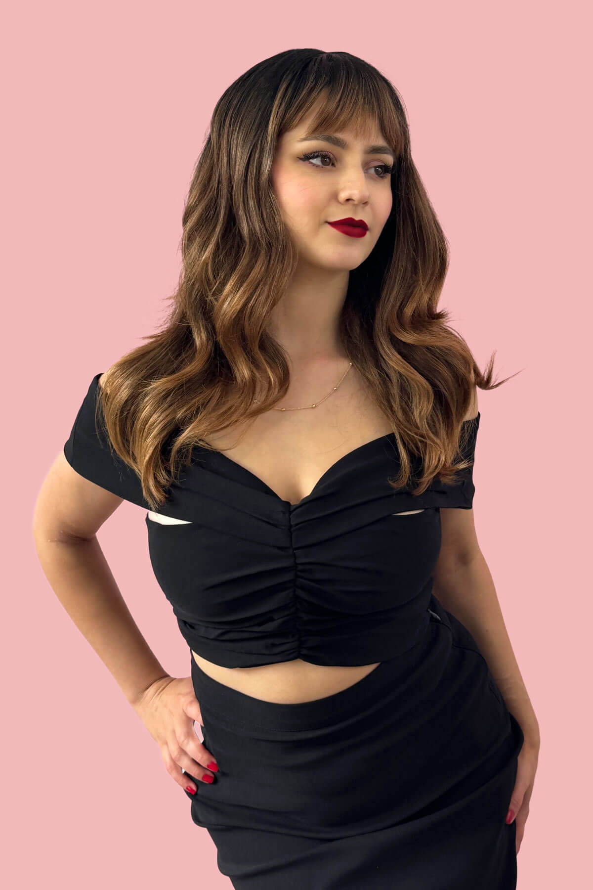Woman wearing a black dress against a pink background. Ombre brown wig with reddish brown highlights & waves: Serenity