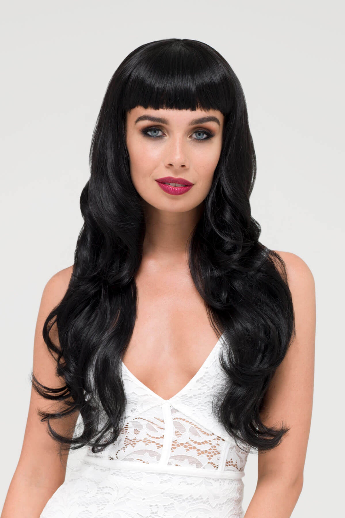 Woman with long black wig and white lace top on a light gray background. Long wavy black wig with vintage-style, rockabilly, straight fringe: Eloise