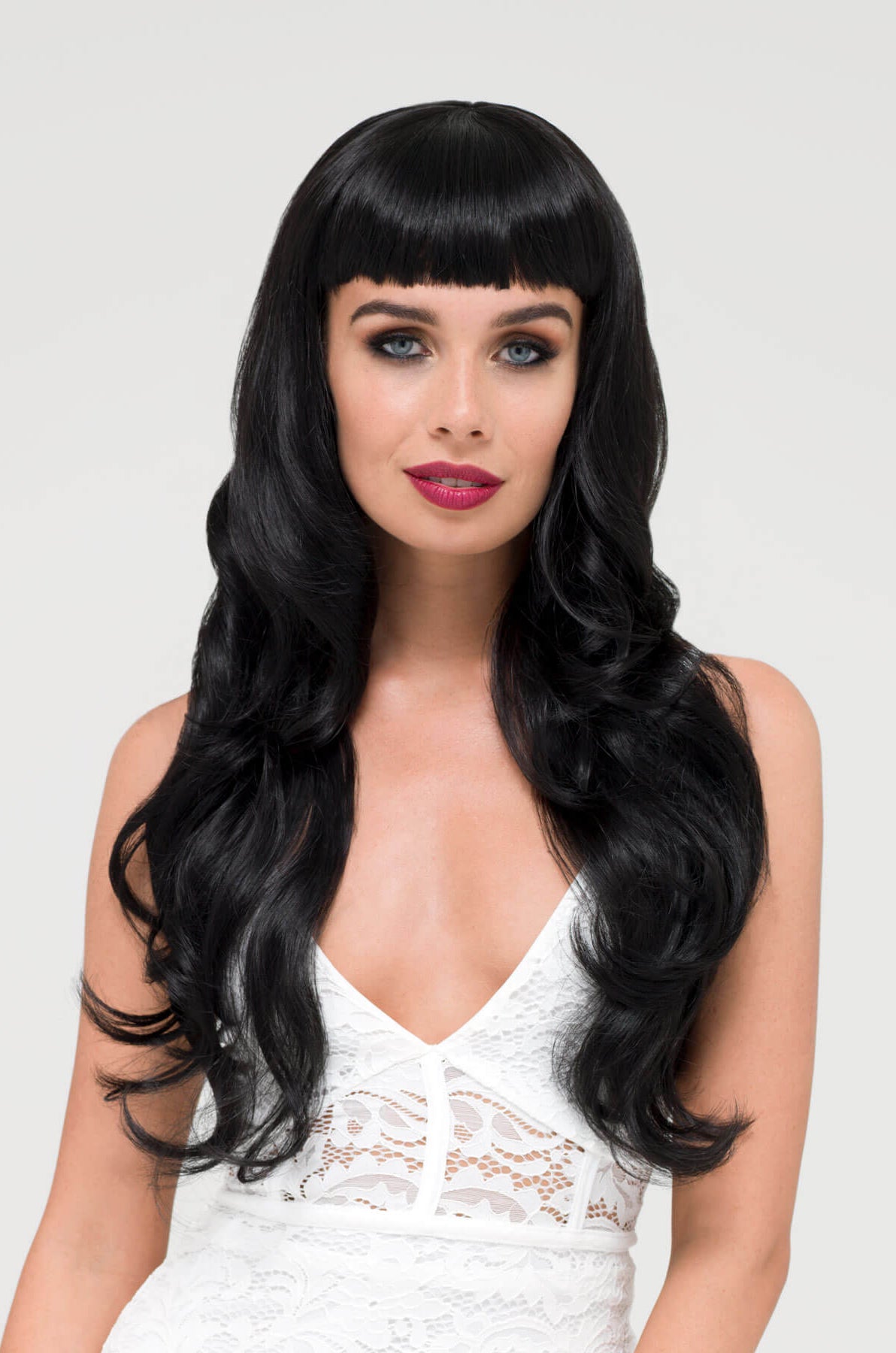 Woman with long black wig and white lace top on a light gray background. Long wavy black wig with vintage-style, rockabilly, straight fringe: Eloise