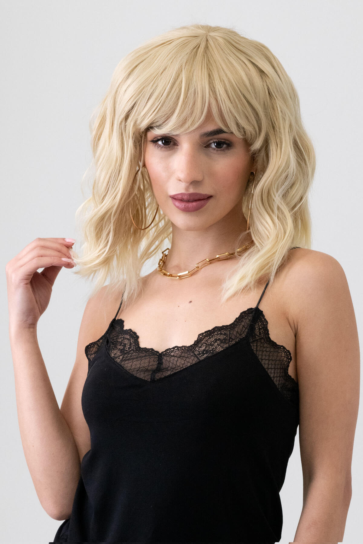 Woman wearing a blonde wig and black lace top against a plain background. Long blonde bob wig (LOB) with textured waves: Kara