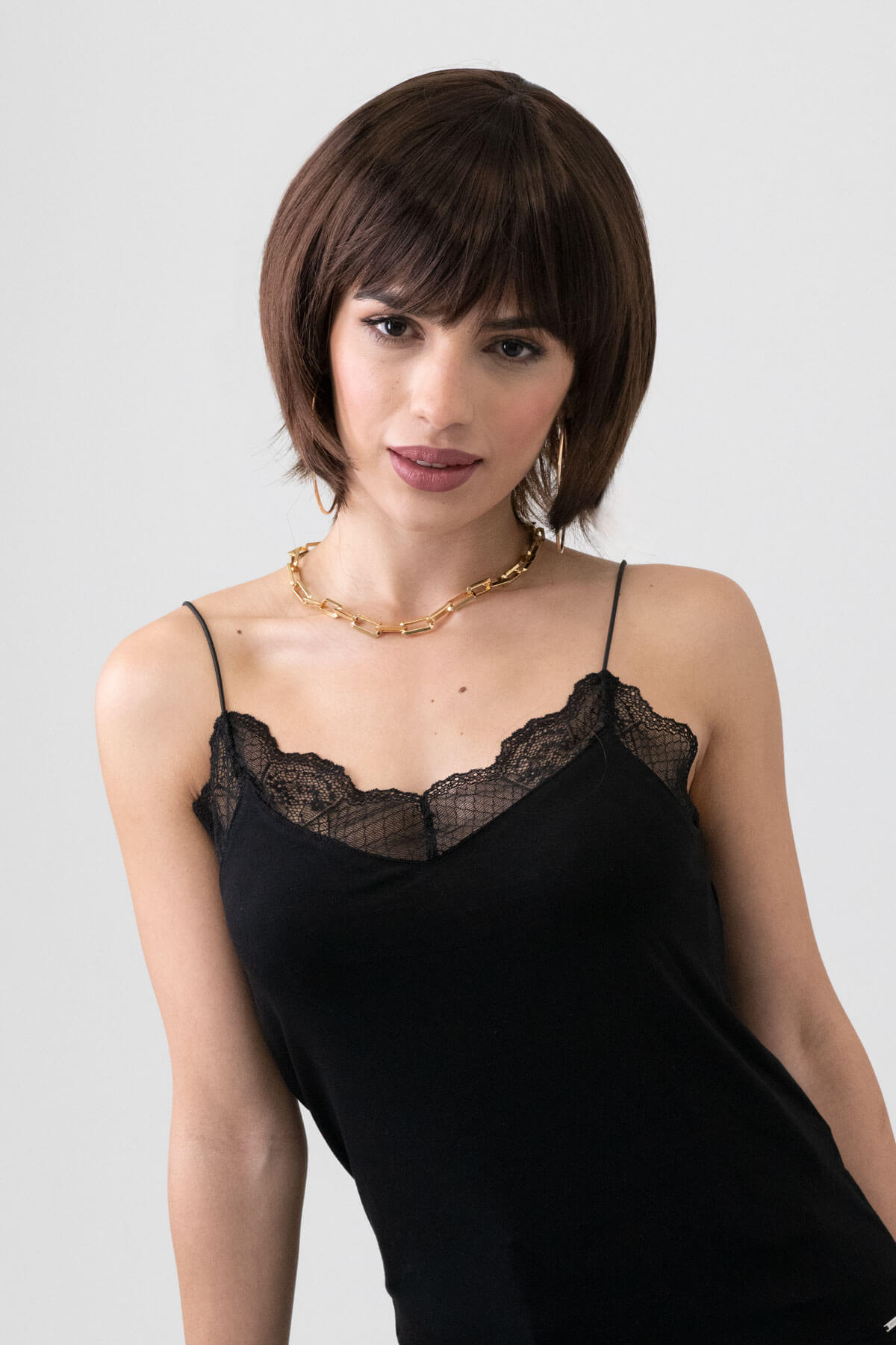 Woman wearing a black lace camisole against a plain background. Dark brown pixie cut wig with reddish brown lowlights: Cierra