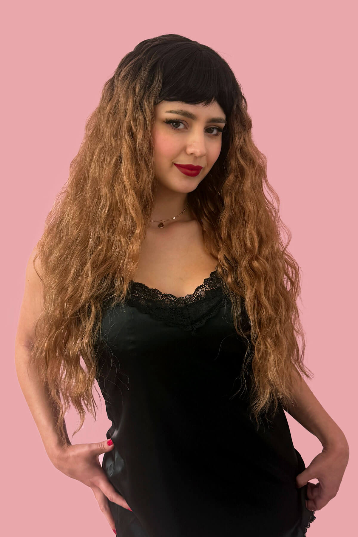 Woman with long wavy hair wearing a black dress against a pink background. Long wig with crimped mermaid waves: Astrid brown and blonde 4TN27