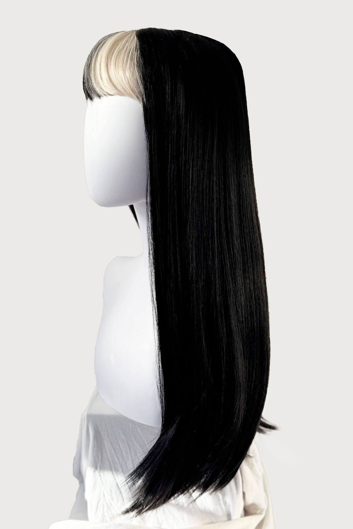 Long black wig with a blonde section on a mannequin head against a white background. Long, black, straight wig with platinum fringe streak and retro, straight fringe: Imogen