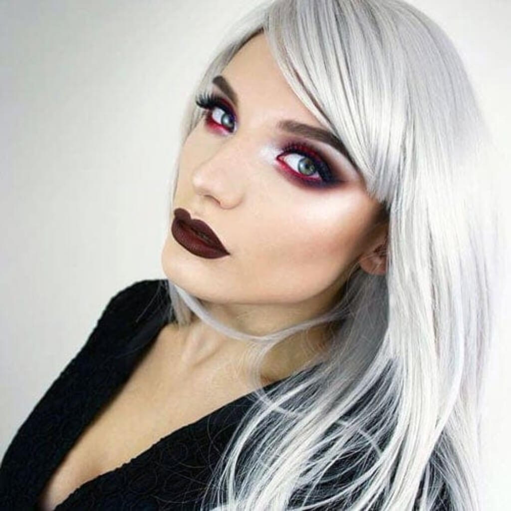 Person with white hair and dramatic makeup against a plain background. Long silver/grey wig in razor cut, face framing style: London