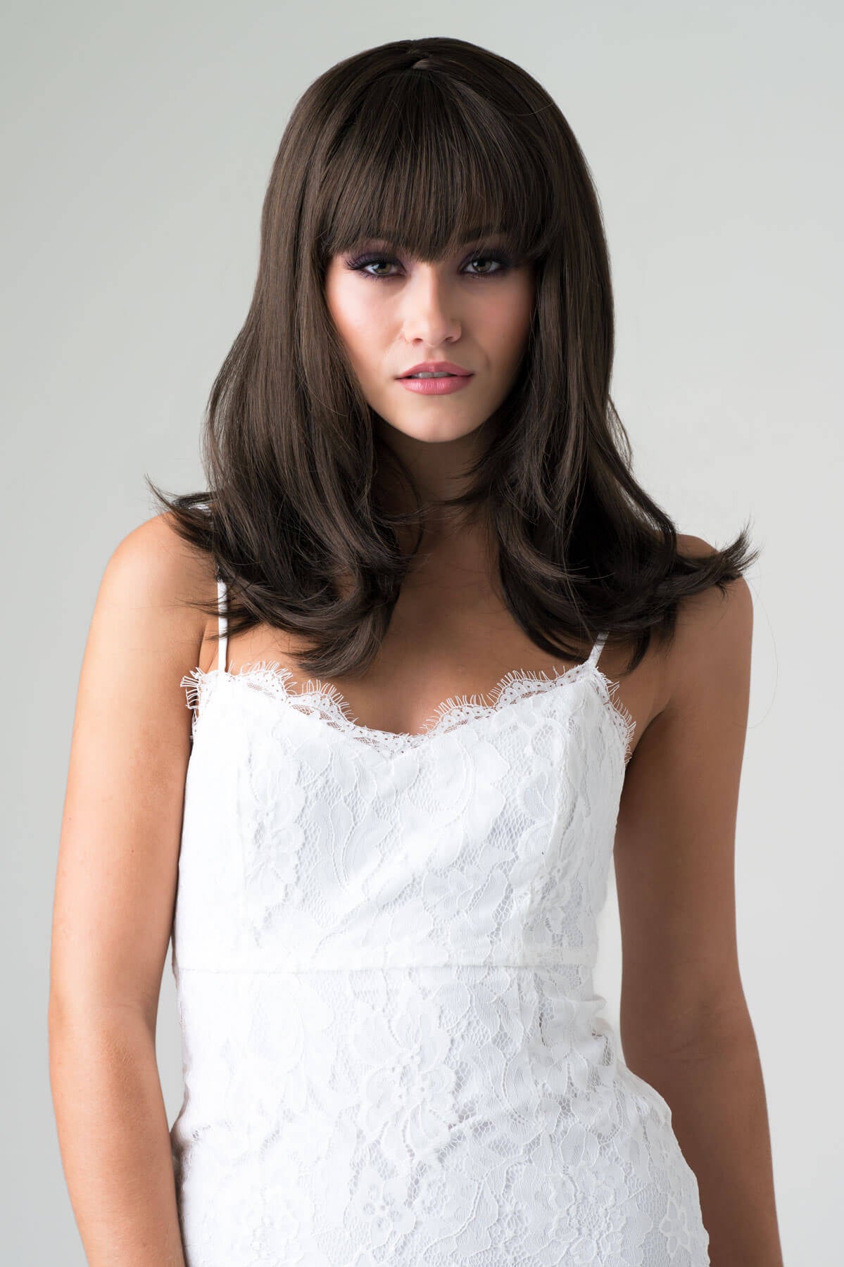 Woman wearing a white lace dress with a plain background. Brown long bob wig, layered with straight fringe: Katia chestnut brown 8