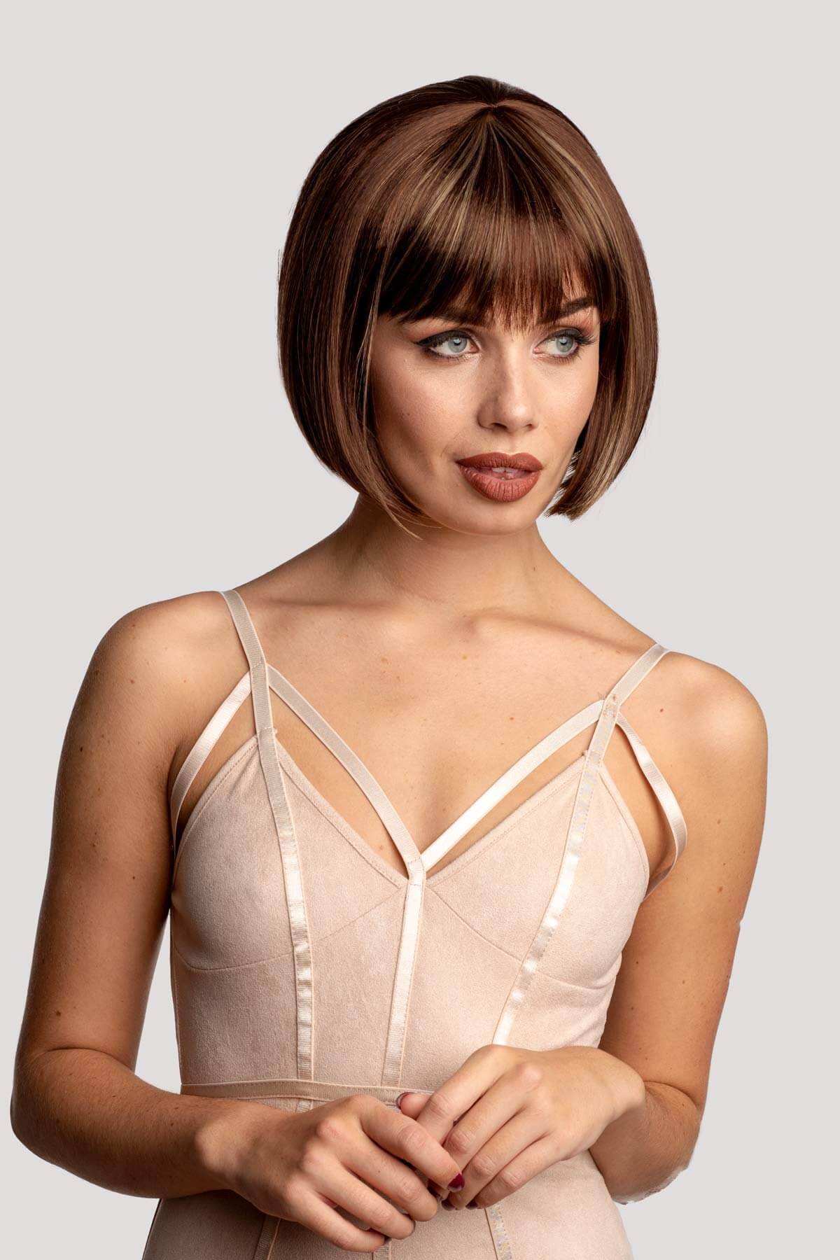 Woman wearing a beige strappy top against a plain background. Brown bob wig with blonde highlights: Bethany