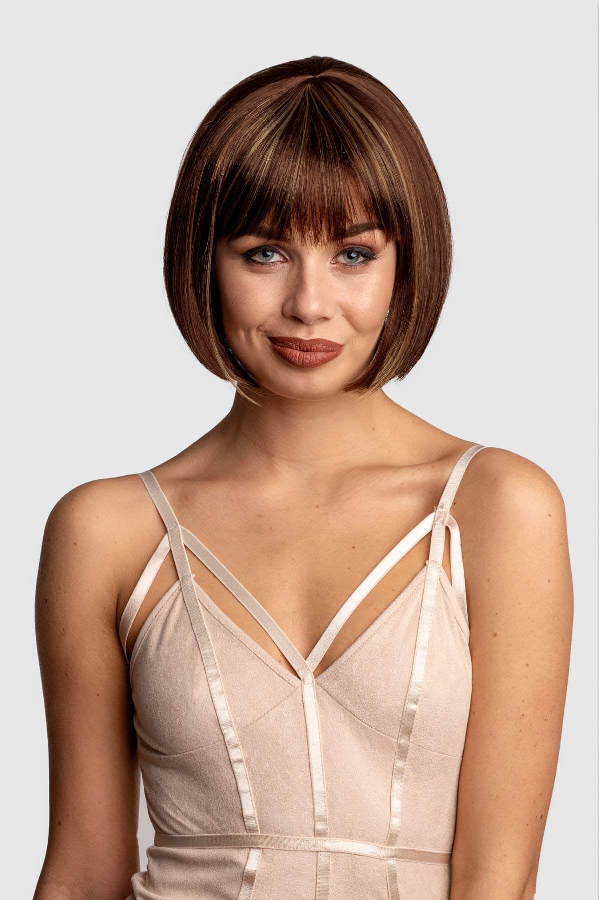 Woman with a stylish haircut wearing a beige dress against a plain background. Brown bob wig with blonde highlights: Bethany