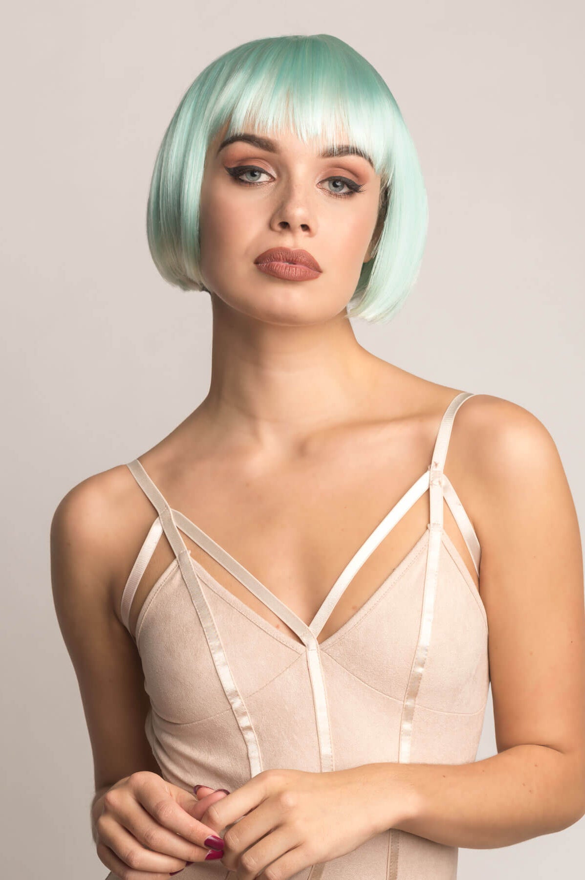 Woman with a stylish haircut wearing a beige satin dress against a plain background. Turquoise bob wig, with platinum blonde ombre, short and chic: Eunice