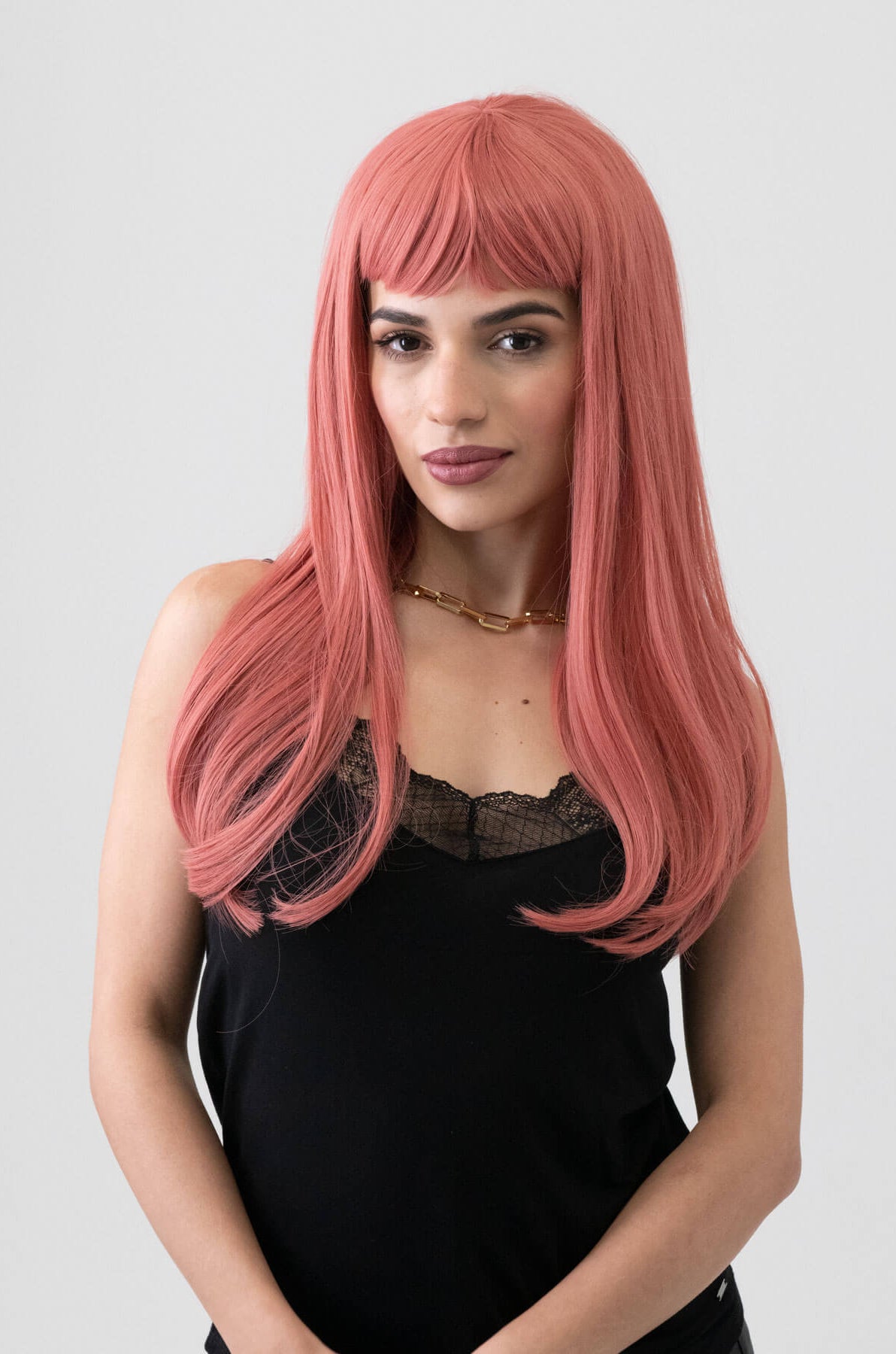 Woman with long pink wig wearing a black top on a white background. Long Pink Wig With Short, Straight Fringe: Stephanie