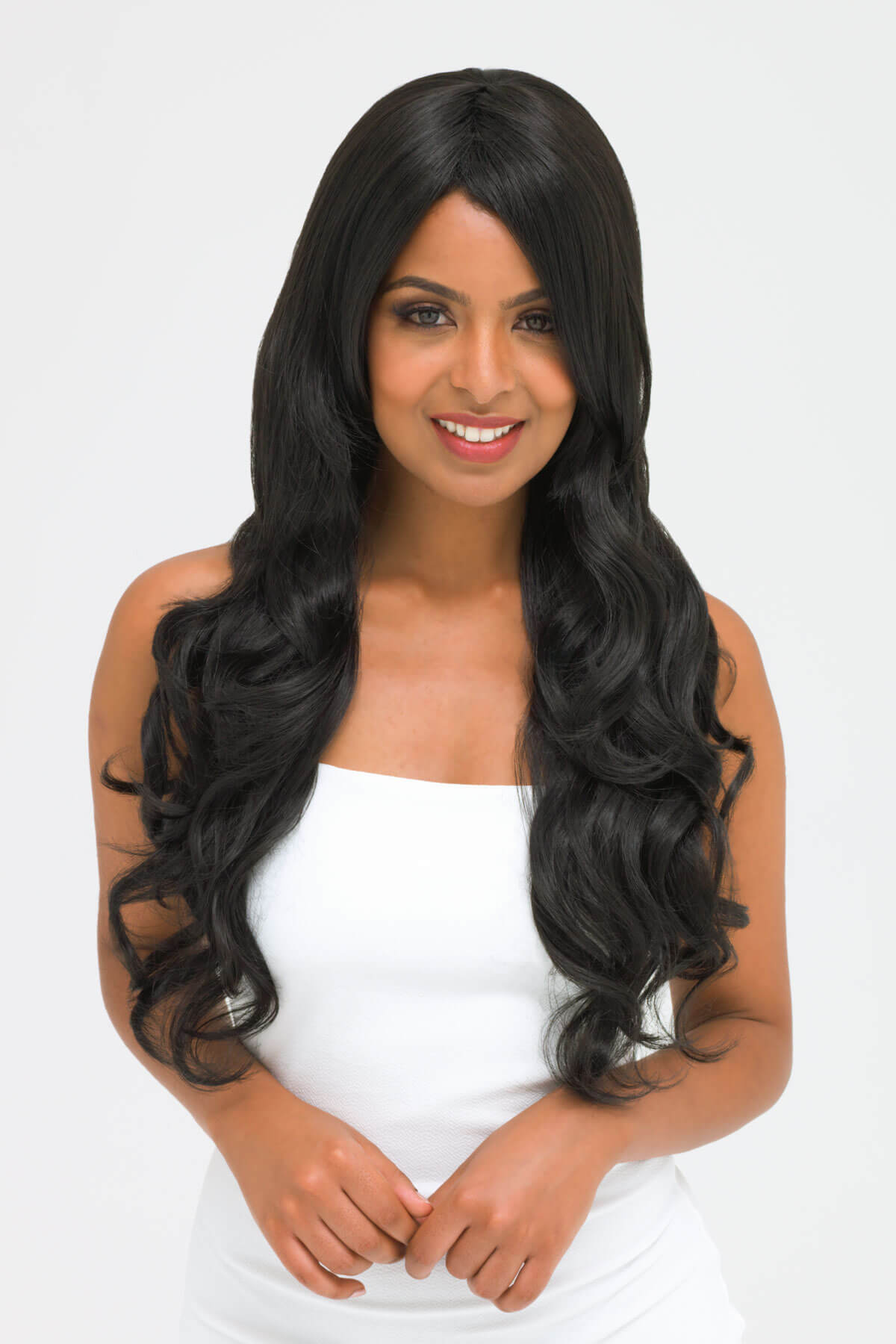 Woman with long black wavy hair wearing a white top on a light gray background. Long wavy black wig with side-sweeping Fringe: Charlotte