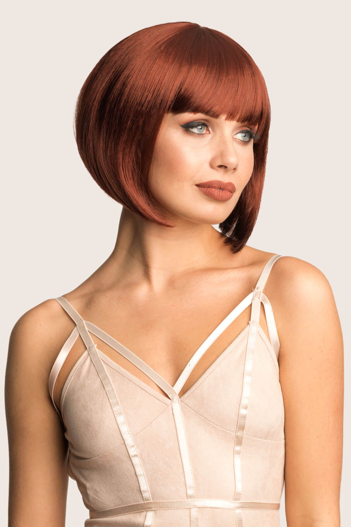 Woman with a stylish haircut wearing a beige dress against a plain background. Ginger/Copper red bob wig, Inverted / A-Line style: Jacqueline