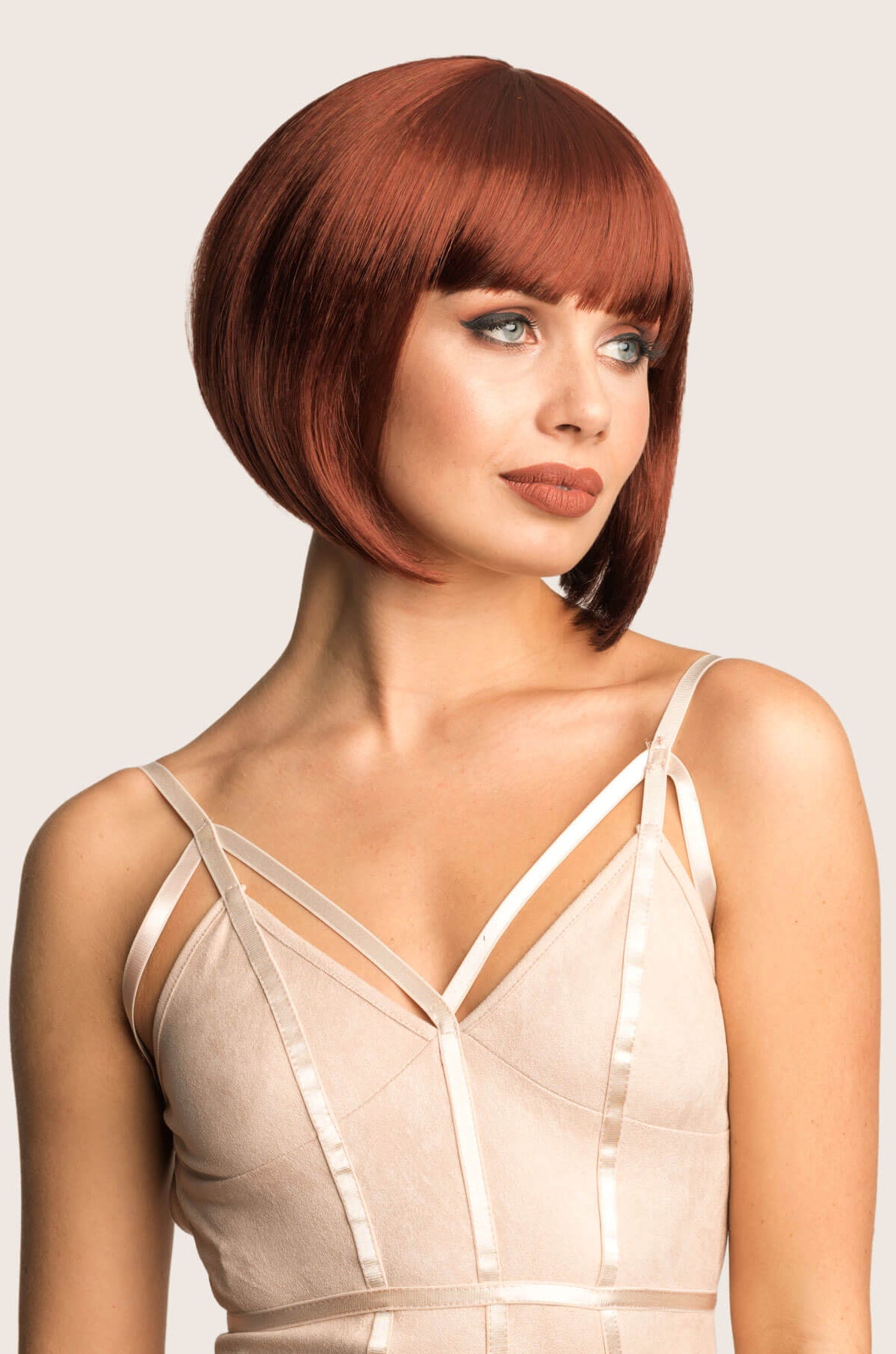 Woman with a stylish haircut wearing a beige dress against a plain background. Ginger/Copper red bob wig, Inverted / A-Line style: Jacqueline