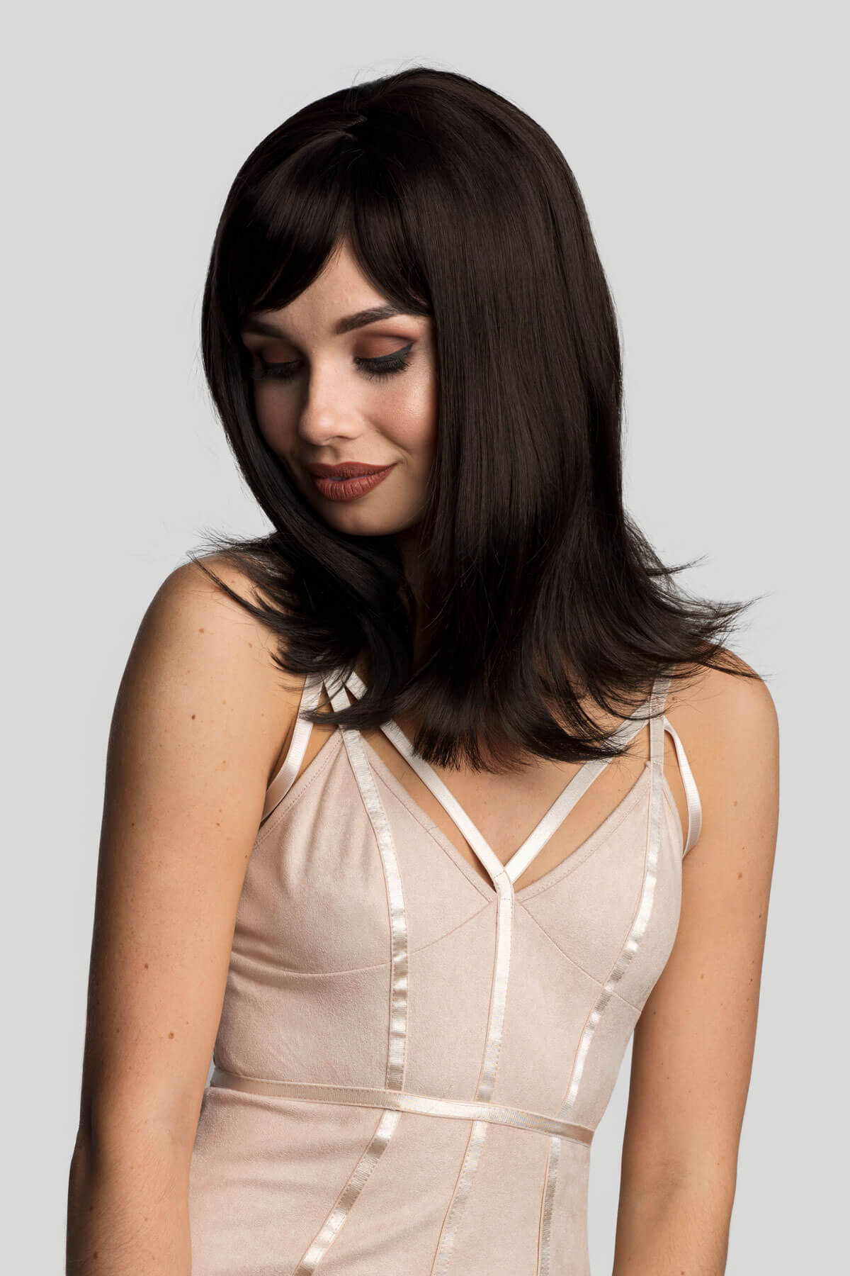 Woman wearing a beige dress with thin straps against a light gray background. Brown long bob wig, layered with straight fringe: Katia dark brown 2