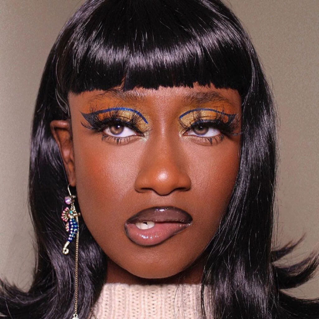 Close-up of a person with bold makeup and black hair against a neutral background. Black long bob wig with a short retro-style fringe: Beth