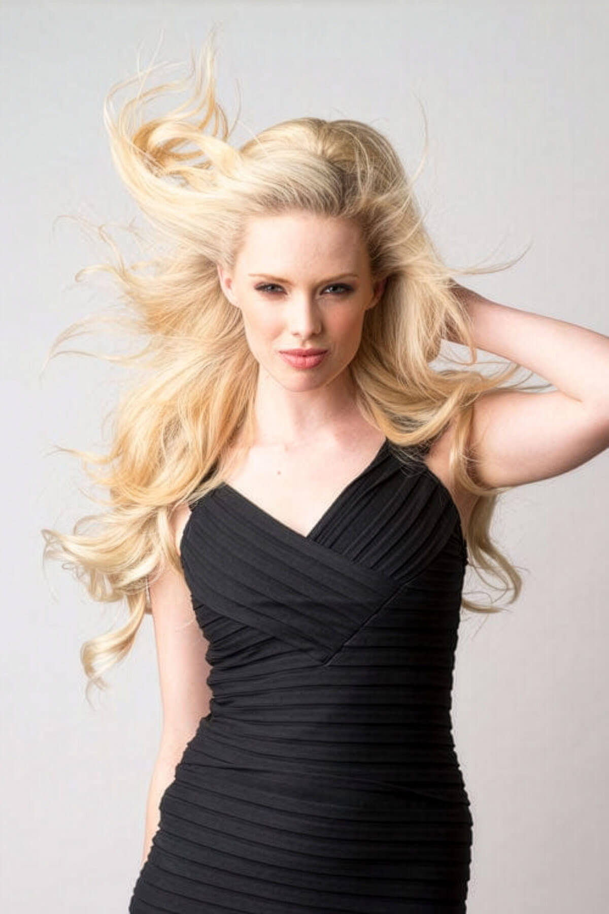 Woman in a black dress with flowing blonde hair against a light gray background