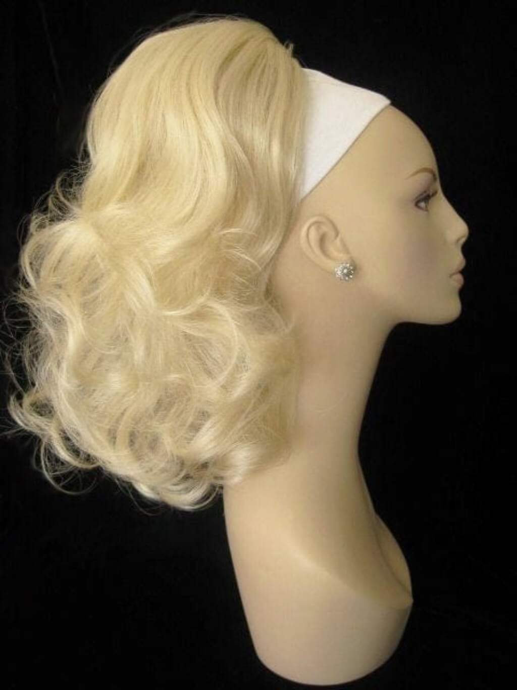 Blonde wig on a mannequin head against a black background. Curly ponytail extension clip-on hairpiece: Tulisa blonde 613