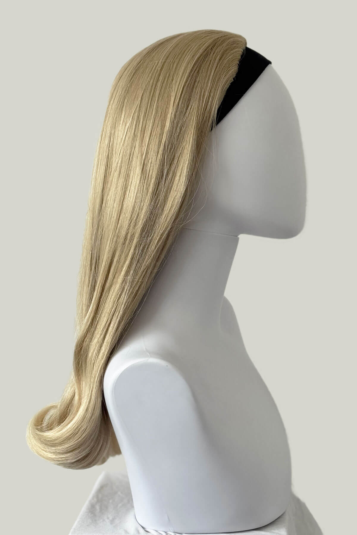 Blonde wig on a mannequin head against a plain background. 1960s Retro high crown, half wig hairpiece, long with hair flip: Priscilla blonde 613T24