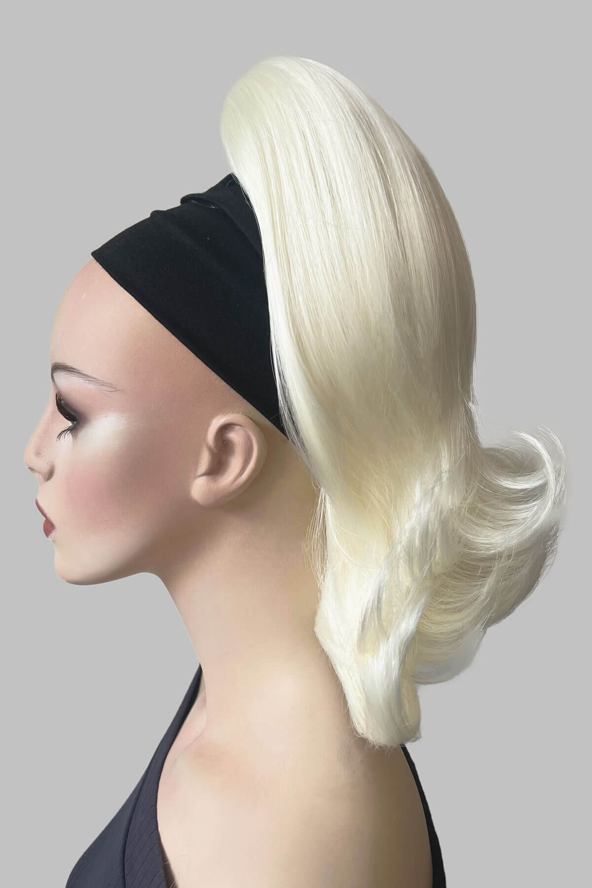 Mannequin head with a blonde wig and black headband on a gray background. Ponytail hairpiece, shoulder length with flick/flip, retro 1960s style: Ariana Platinum blonde 1001