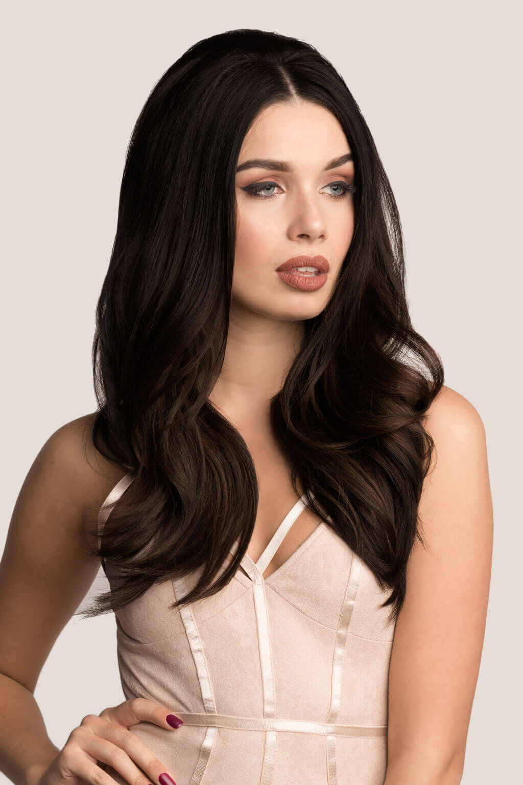 Woman with long, dark brown hair wearing a beige dress against a light gray background. Volume and Height Booster Hairpiece: Blaise black 1B