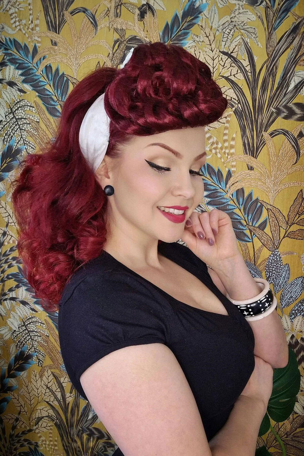Woman with red hair styled in a vintage fashion against a decorative wallpaper background. Hair poodle clip-in hairpiece bun vintage style 1950s: Lucille cherry red 39