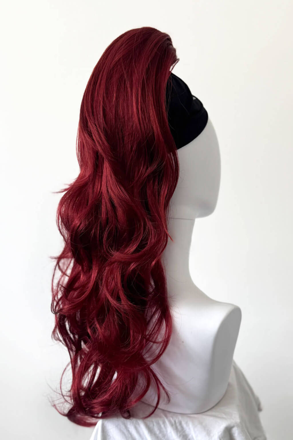 Red wig on a mannequin head against a white background. Clip-in ponytail hairpiece extension: Olivia Red 350-39