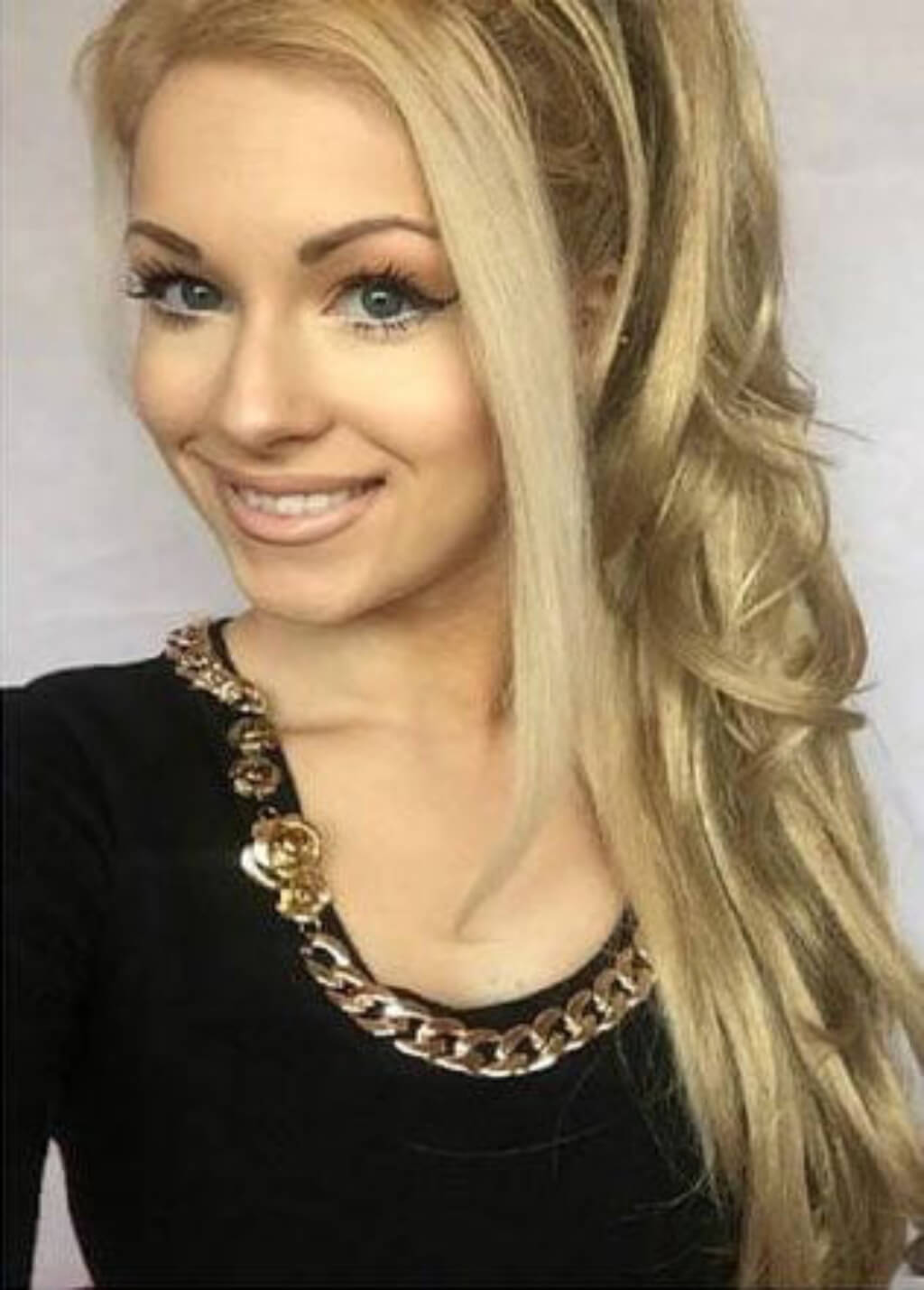 Woman with blonde hair and a gold necklace against a plain background. Clip-in ponytail hairpiece extension: Olivia blonde 613T24