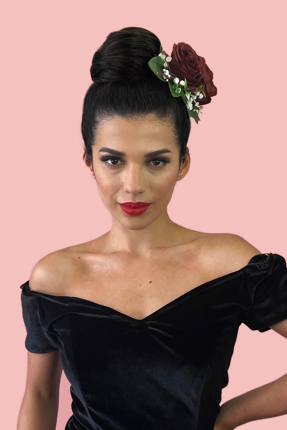Woman in a black off-shoulder dress with a floral hairpiece against a pink background. Hairpiece bun; instant perfect bun hairpiece: Hepburn black 1b