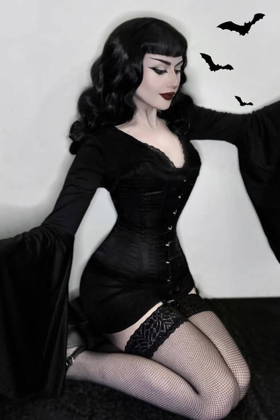 Woman in a black corset and stockings with bats in the background. 1950s style half wig hairpiece with beautiful waves: Morgana jet black 