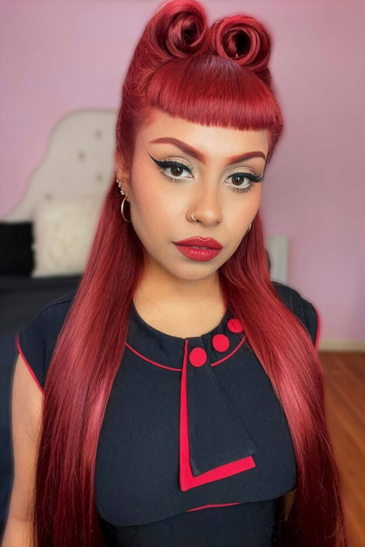 Woman with red hair styled in two victory rolls wearing a black outfit with red accents. 