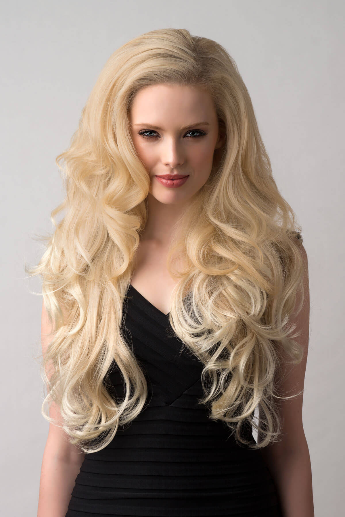 Woman with long blonde hair wearing a black top on a gray background. Long blonde 3/4 hairpiece (half wig), big loose curls: Zara blonde 613T24