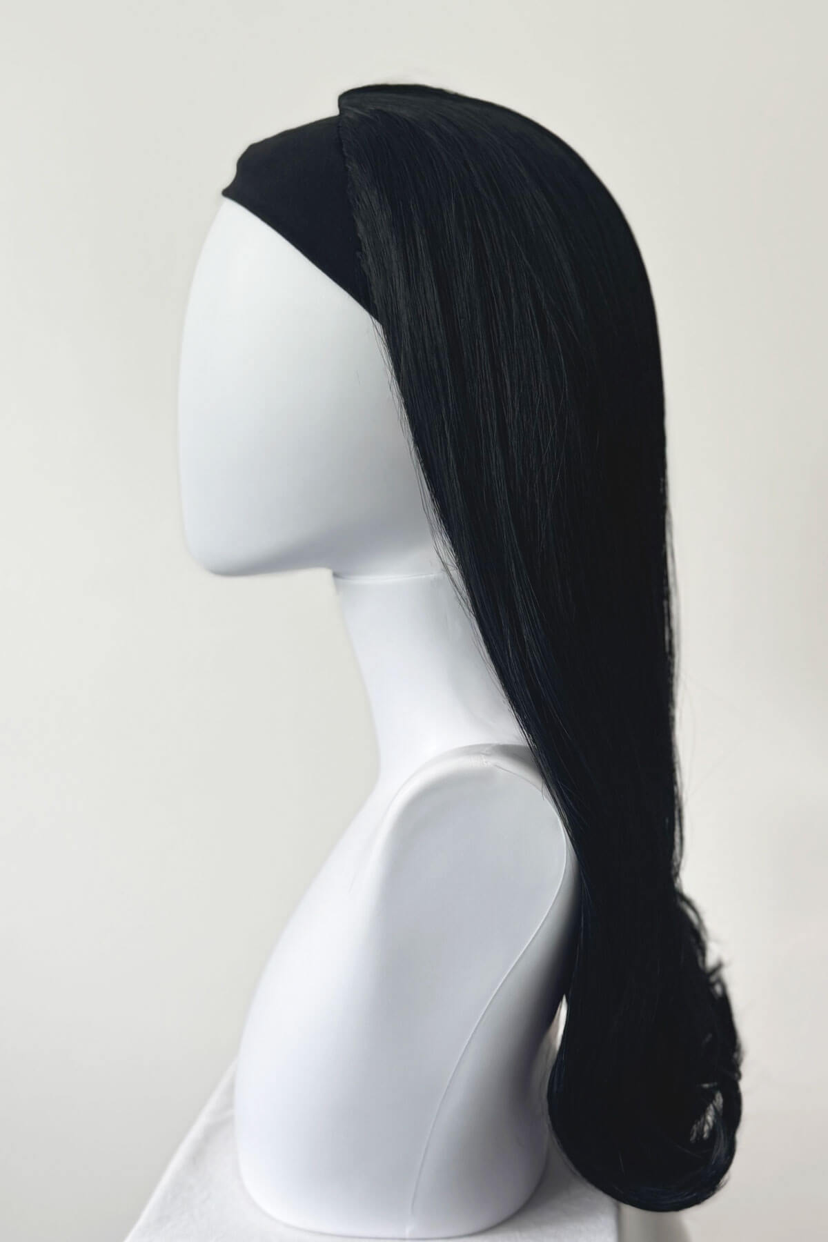 Black wig on a white mannequin head against a white background. 1960s Retro high crown, half wig hairpiece, long with hair flip: Priscilla jet black 1