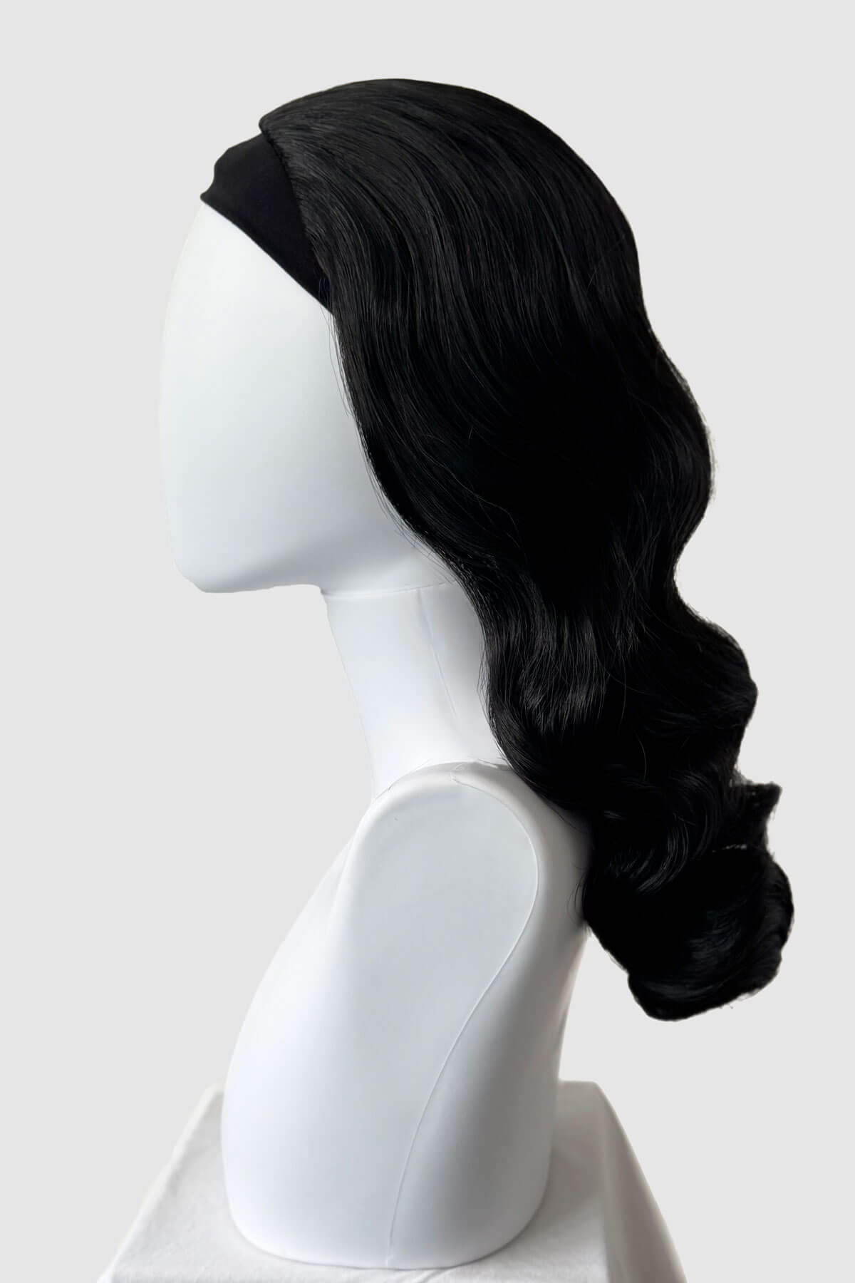 Black wig on a white mannequin head against a white background. 1950s style half wig hairpiece with beautiful waves: Morgana black 1b