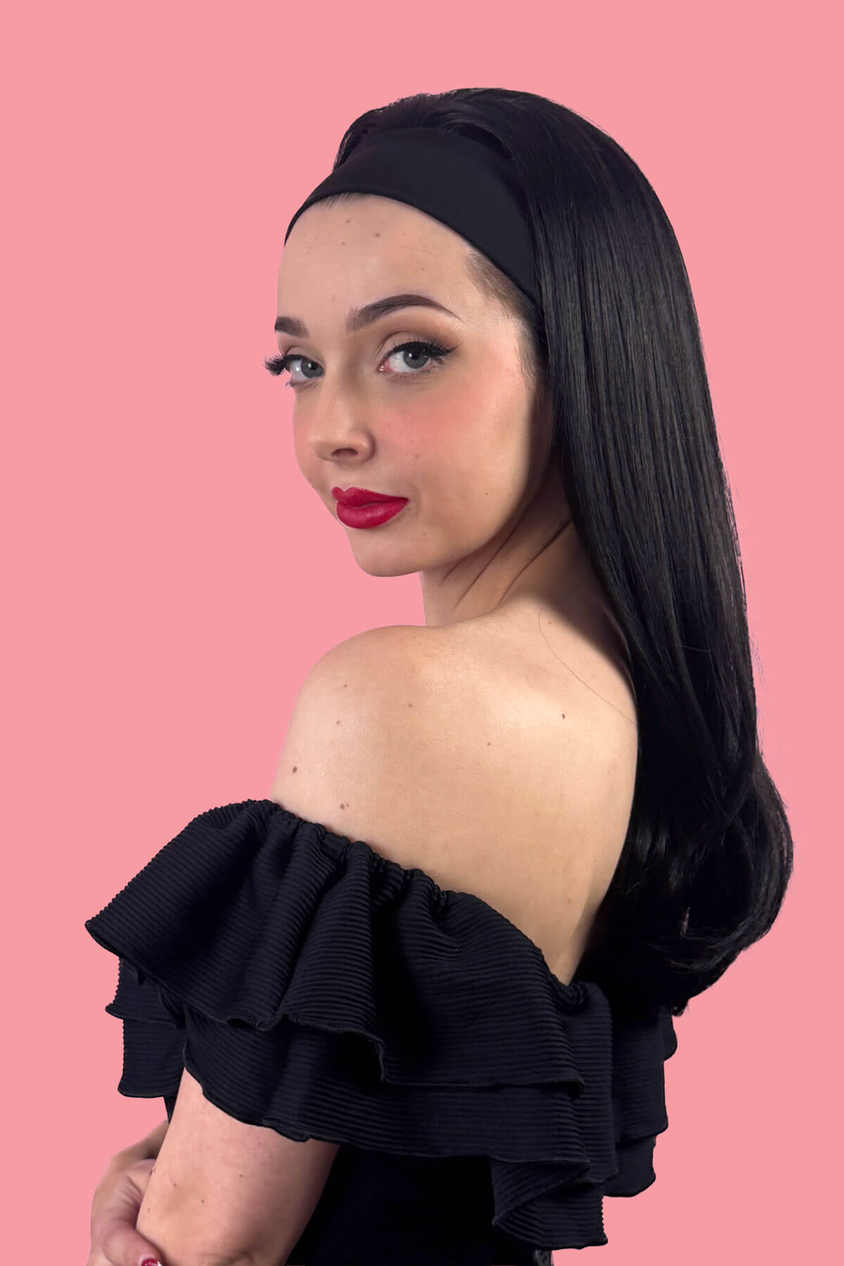Woman with long black hair with a headband in it wearing a black off-shoulder top against a pink background. Headband half wig hairpiece, long and straight: Isla black 1B