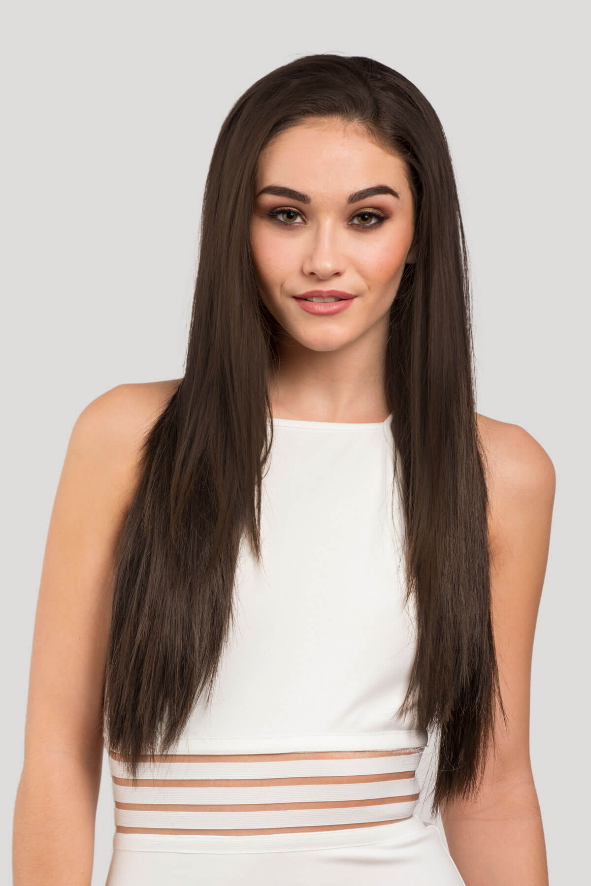 Woman with long straight hair wearing a white dress on a light gray background. Straight brown half wig hairpiece extension, long: Faye dark brown 6
