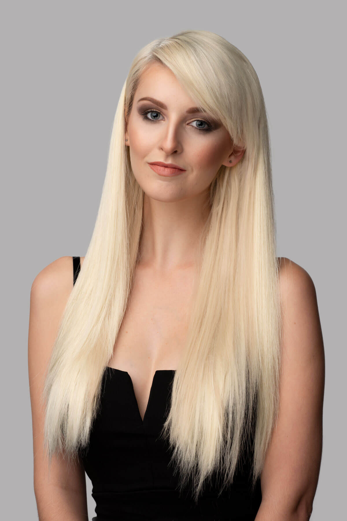 Woman with long blonde hair wearing a black top against a gray background