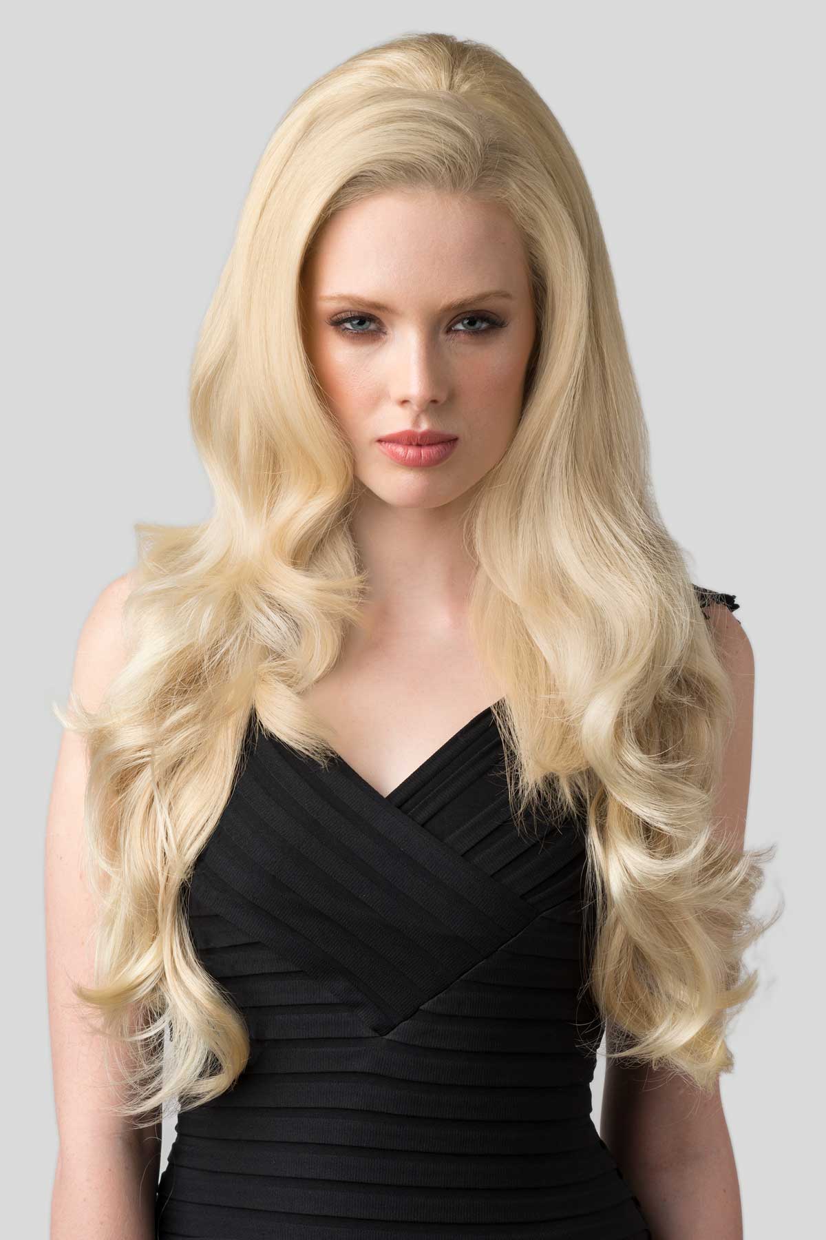 Woman with long blonde hair wearing a black dress on a gray background. Half wig with volume booster/height booster: Corrine blonde 613T24