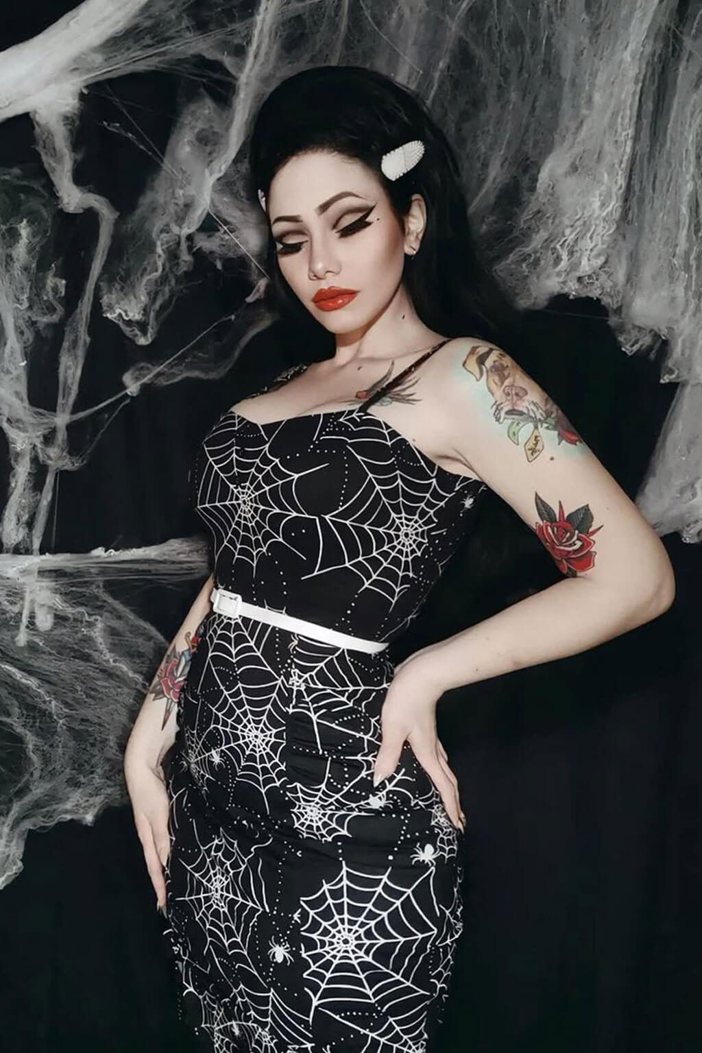 Woman in a black dress with spider web pattern against a dark background. High crown long, wavy half wig and volume ring: Bardot jet black 1