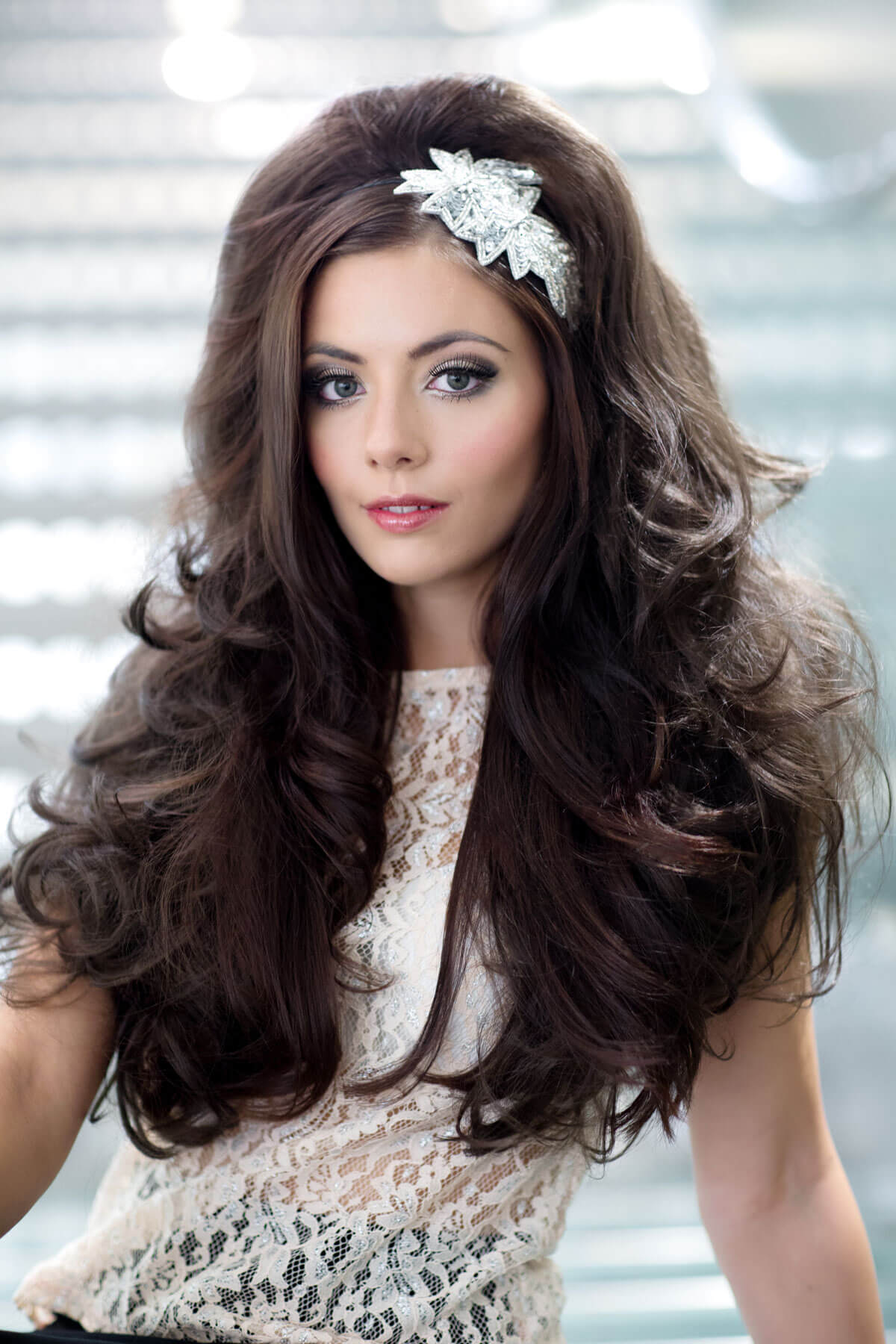 Woman with long, wavy hair wearing a decorative headband against a blurred indoor background