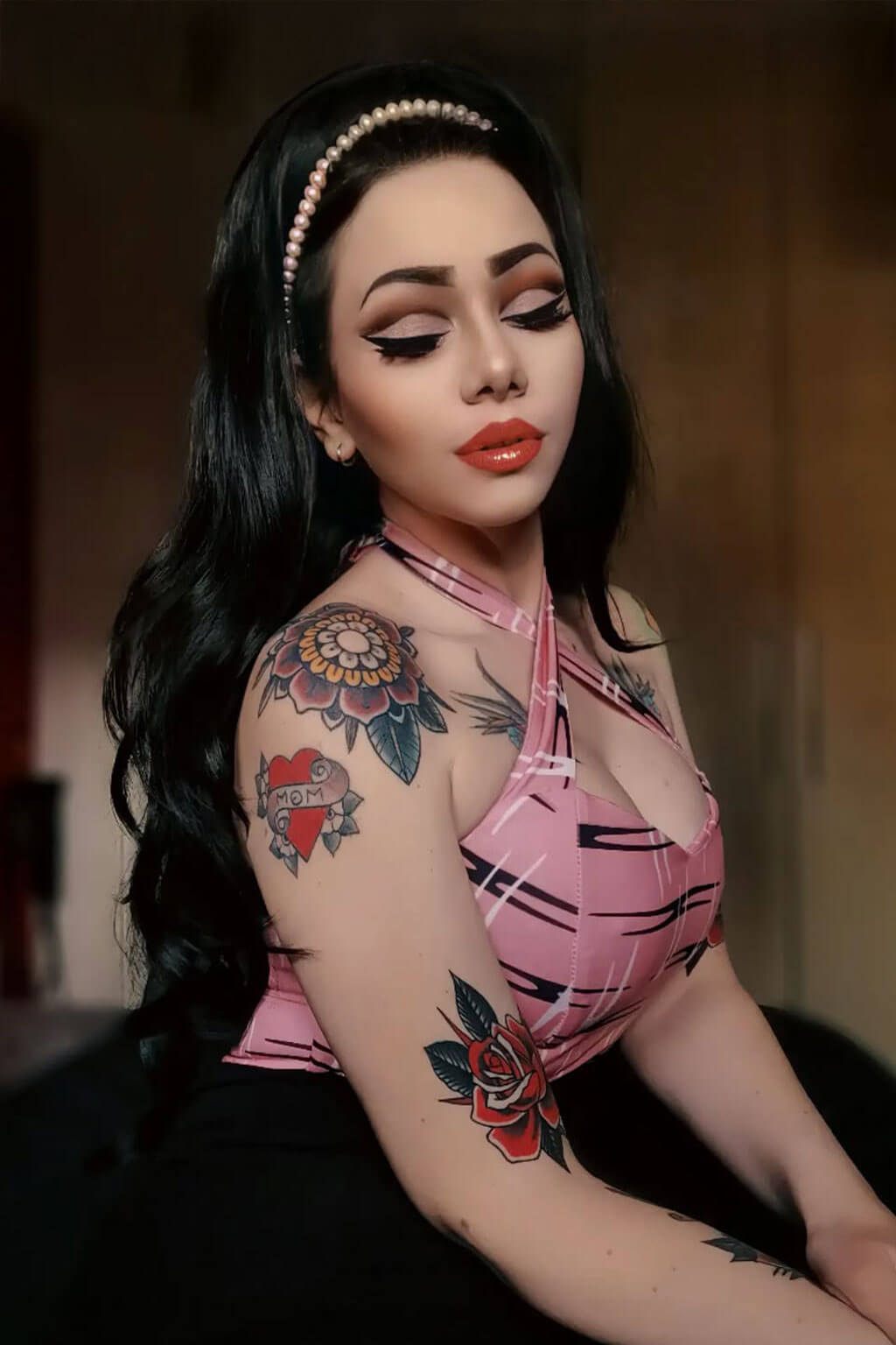 Woman with tattoos wearing a pink top against a blurred background - High crown long, wavy half wig and volume ring: Bardot black 1B