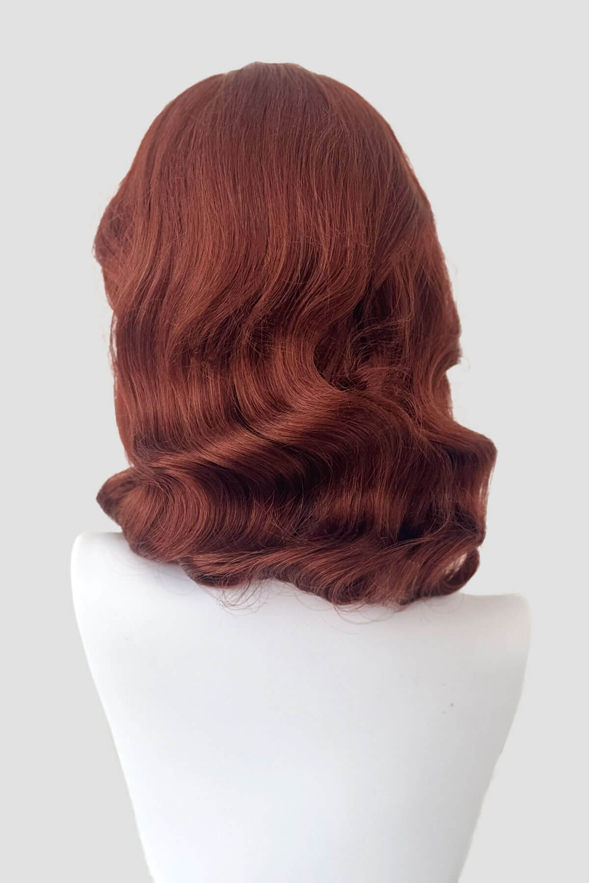 Reddish-brown wig on a mannequin head against a white background. 1940s style half wig hairpiece with beautiful marcel waves: Virginia copper red 130